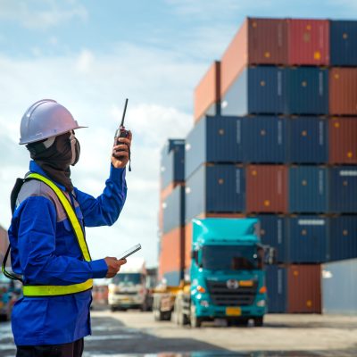 Foreman using and talking walkie talkie to control loading Containers box to truck at Container depot station for Logistic Import Export Background. Business logistic concept